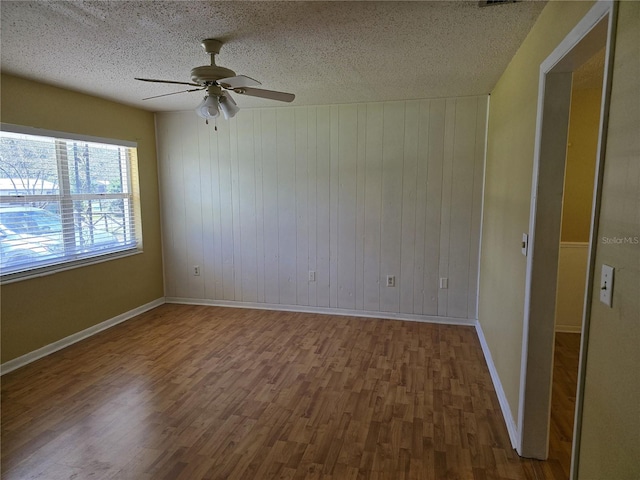 unfurnished room with ceiling fan, a textured ceiling, baseboards, and wood finished floors