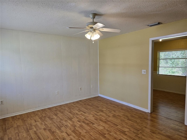 spare room with a textured ceiling, wood finished floors, visible vents, baseboards, and a ceiling fan