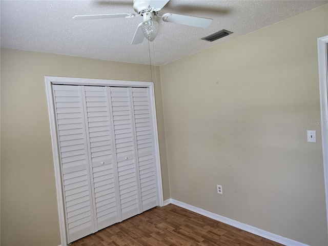 unfurnished bedroom with a closet, visible vents, a textured ceiling, wood finished floors, and baseboards