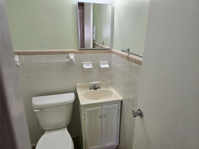 half bathroom with toilet, a wainscoted wall, tile walls, and vanity