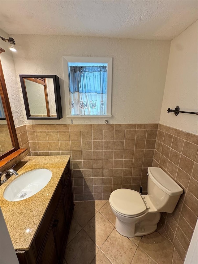 bathroom with a textured ceiling, toilet, vanity, tile walls, and tile patterned floors