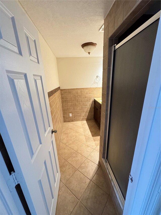 bathroom with a stall shower, tile patterned flooring, tile walls, and a textured ceiling