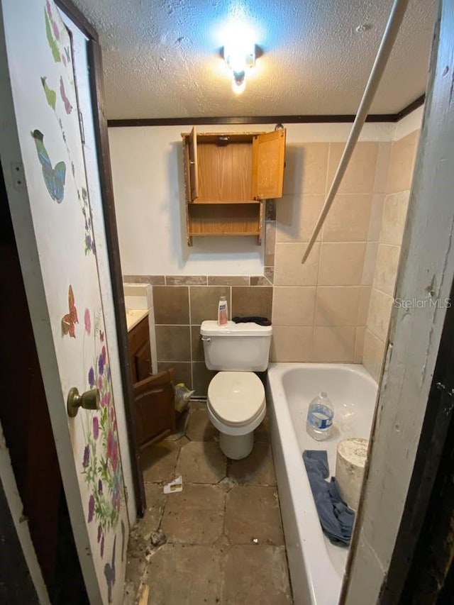 bathroom with a textured ceiling, toilet, tile walls, and vanity