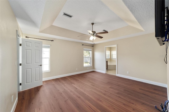 unfurnished bedroom featuring a textured ceiling, wood finished floors, visible vents, baseboards, and a raised ceiling