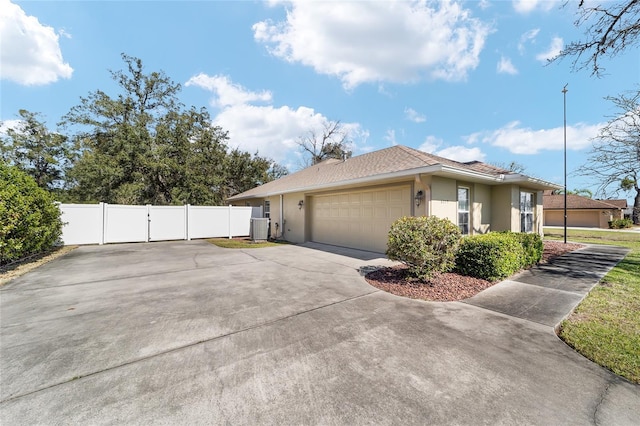 view of property exterior featuring an attached garage, central air condition unit, fence, driveway, and stucco siding