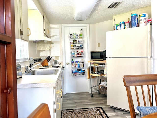 kitchen with light hardwood / wood-style floors, white refrigerator, sink, and a textured ceiling