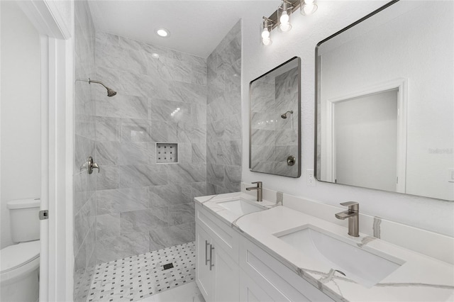 full bathroom featuring toilet, double vanity, a sink, and tiled shower