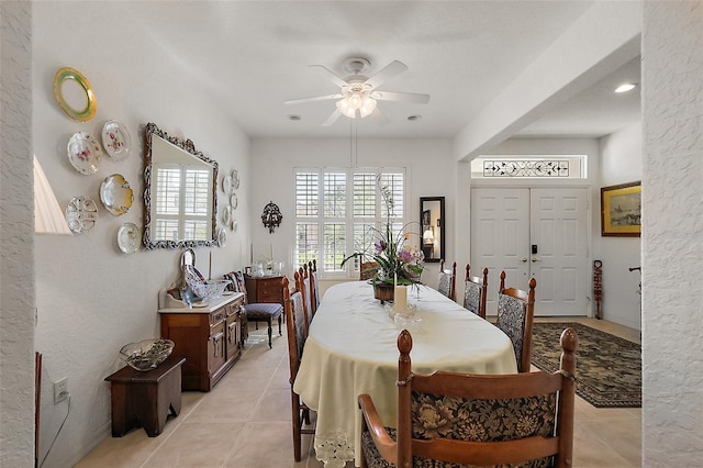 dining area featuring a ceiling fan, a textured wall, and light tile patterned floors