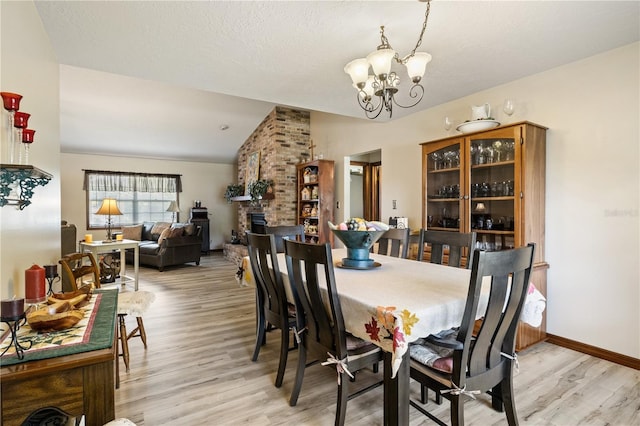 dining room featuring baseboards, light wood-style flooring, an inviting chandelier, vaulted ceiling, and a brick fireplace