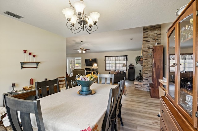 dining space with a textured ceiling, light wood-style flooring, ceiling fan with notable chandelier, and visible vents