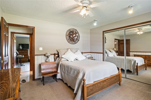 bedroom with a textured ceiling, light carpet, a ceiling fan, a closet, and wainscoting