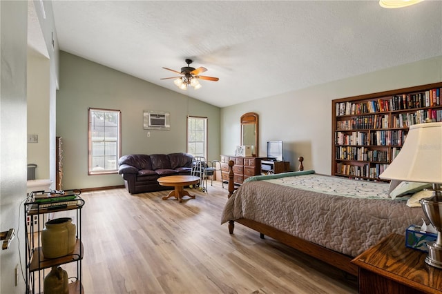 bedroom with a wall unit AC, vaulted ceiling, a textured ceiling, and wood finished floors