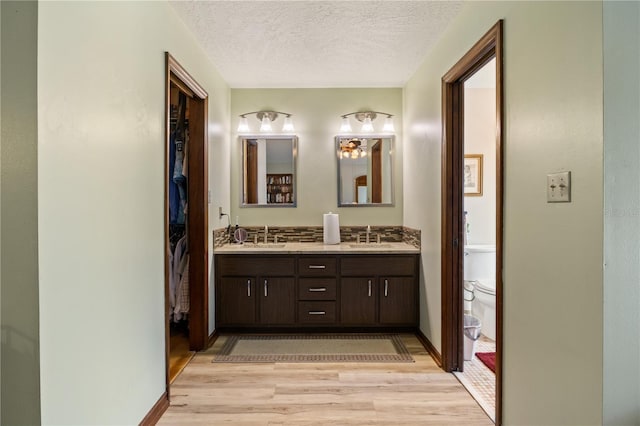 full bathroom with a textured ceiling, toilet, a sink, wood finished floors, and double vanity