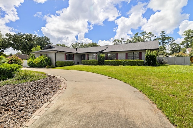 ranch-style home featuring driveway, a front lawn, fence, and brick siding