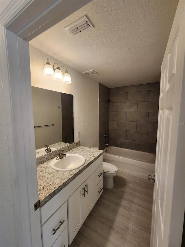 bathroom featuring a textured ceiling, wood finished floors, visible vents, bathing tub / shower combination, and vanity