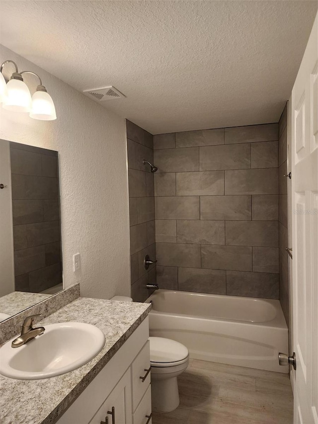 full bathroom featuring a textured wall, toilet, wood finished floors, visible vents, and shower / washtub combination