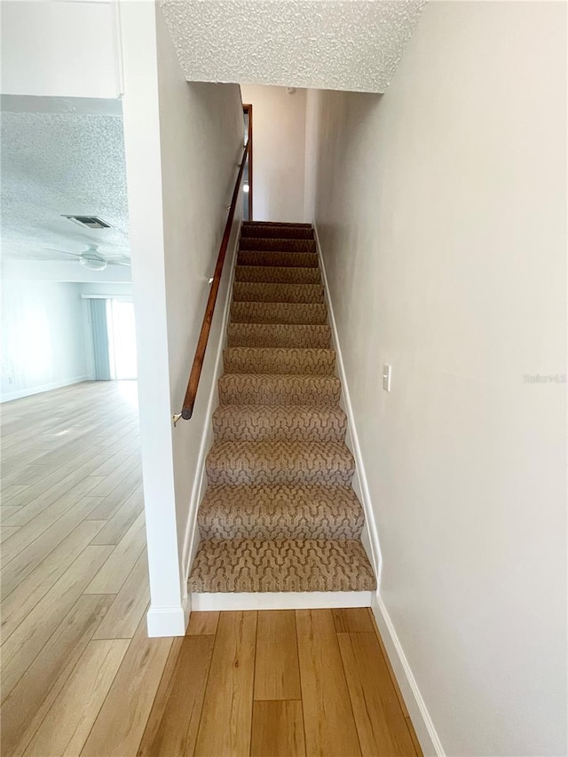 stairway with wood-type flooring and a textured ceiling