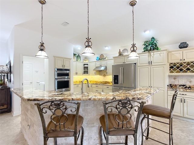 kitchen featuring an island with sink, under cabinet range hood, glass insert cabinets, and stainless steel appliances