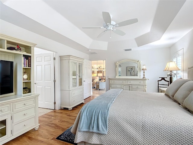 bedroom featuring light wood-type flooring, visible vents, and a tray ceiling