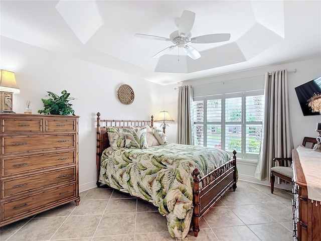 bedroom with a ceiling fan, a tray ceiling, baseboards, and light tile patterned floors