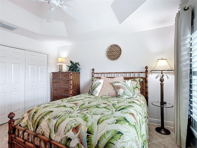 bedroom with a tray ceiling, a closet, visible vents, light tile patterned flooring, and ceiling fan