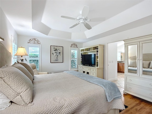 bedroom with ensuite bath, ceiling fan, light wood-style flooring, and a raised ceiling