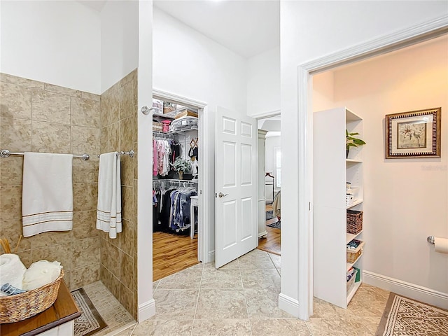 full bath featuring baseboards, a spacious closet, tiled shower, and tile patterned floors