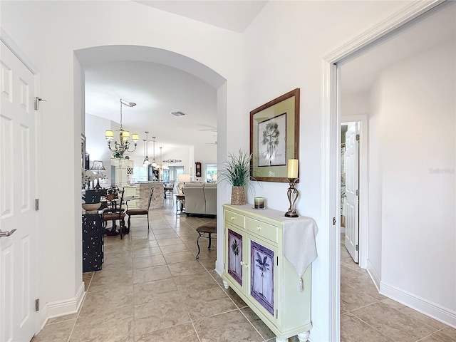 corridor featuring visible vents, baseboards, an inviting chandelier, light tile patterned flooring, and arched walkways