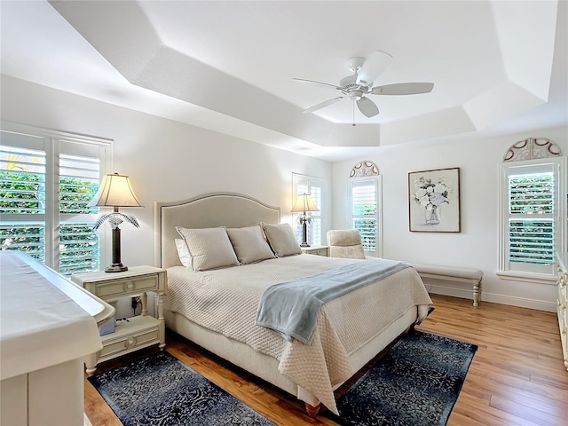 bedroom featuring baseboards, light wood-style floors, a tray ceiling, and a ceiling fan