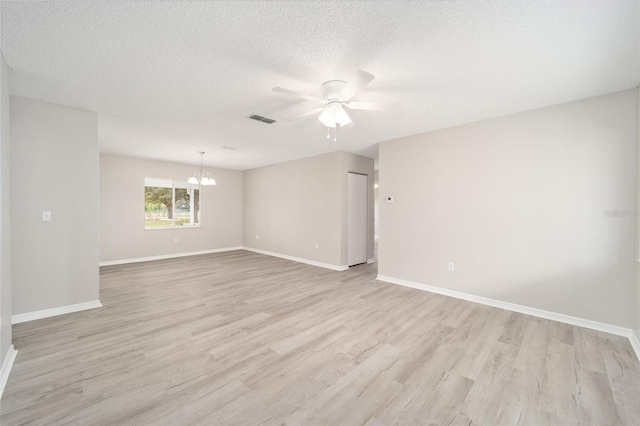 spare room with a textured ceiling, light wood-style flooring, ceiling fan with notable chandelier, visible vents, and baseboards