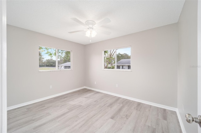 empty room featuring light wood-style floors, a healthy amount of sunlight, a textured ceiling, and baseboards