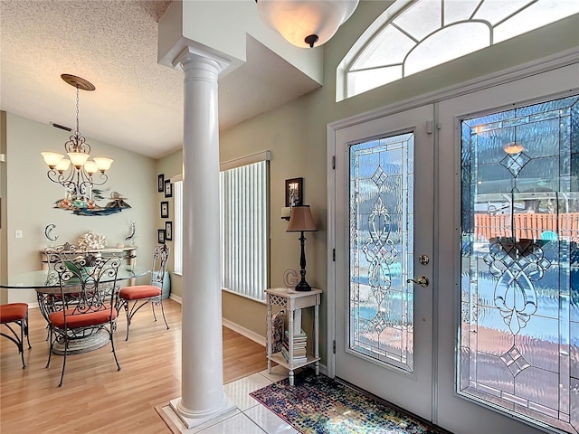 foyer with french doors, light wood finished floors, an inviting chandelier, a textured ceiling, and ornate columns