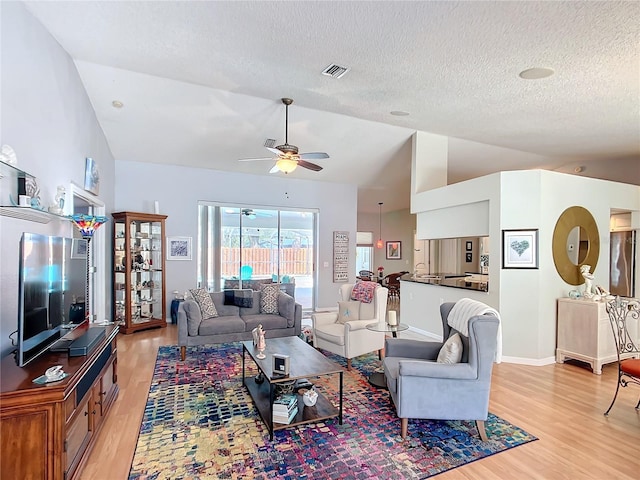 living area with ceiling fan, light wood-style flooring, visible vents, and vaulted ceiling