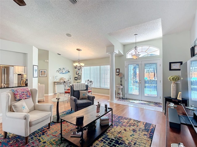 living area with lofted ceiling, a notable chandelier, wood finished floors, french doors, and ornate columns