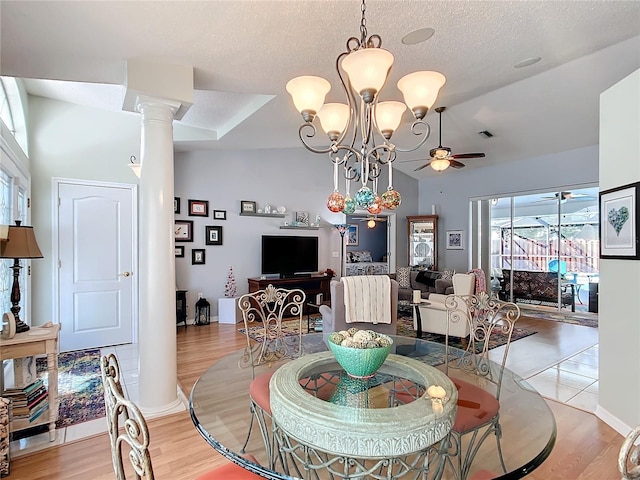 dining room featuring a textured ceiling, ceiling fan with notable chandelier, light wood-style floors, vaulted ceiling, and ornate columns