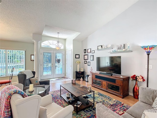 living room with a textured ceiling, vaulted ceiling, french doors, light wood-type flooring, and ornate columns