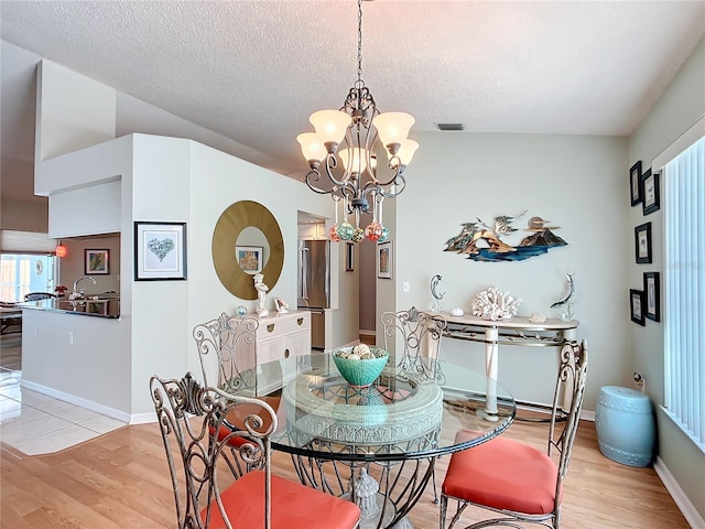 dining room with a textured ceiling, an inviting chandelier, baseboards, and light wood-style floors