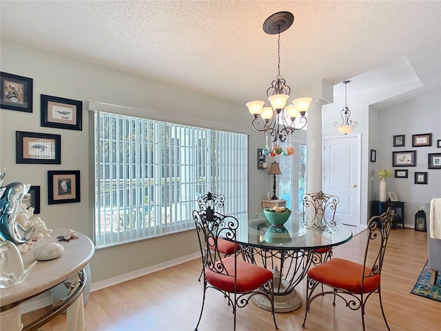 dining room with a textured ceiling, light wood finished floors, a chandelier, and baseboards