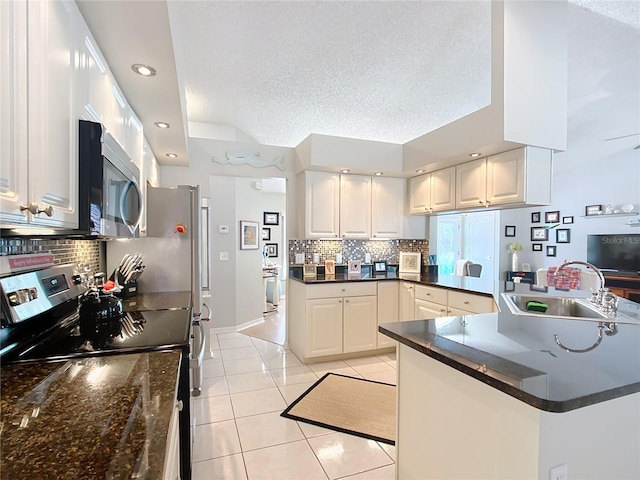 kitchen featuring dark countertops, appliances with stainless steel finishes, white cabinets, a sink, and a peninsula