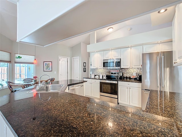 kitchen with stainless steel appliances, dark stone countertops, a sink, and white cabinetry