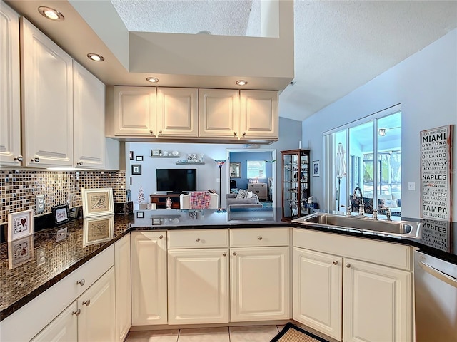 kitchen with white cabinets, backsplash, a peninsula, a sink, and stainless steel dishwasher