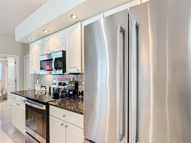 kitchen with light tile patterned floors, stainless steel appliances, backsplash, white cabinets, and dark stone counters