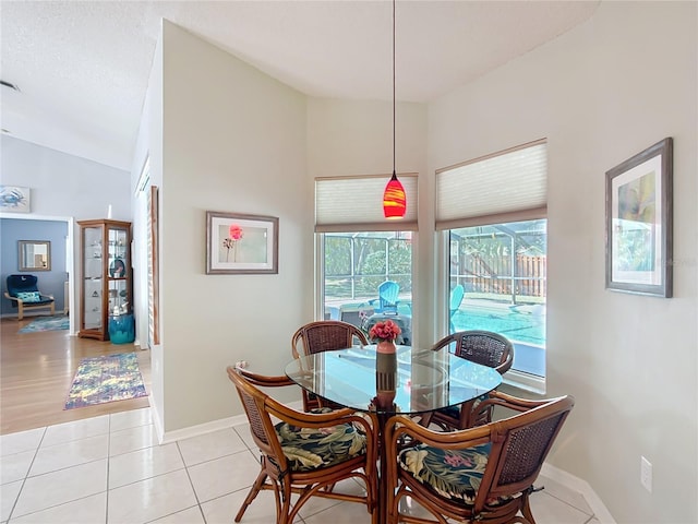 dining space featuring light tile patterned floors, lofted ceiling, a sunroom, a textured ceiling, and baseboards