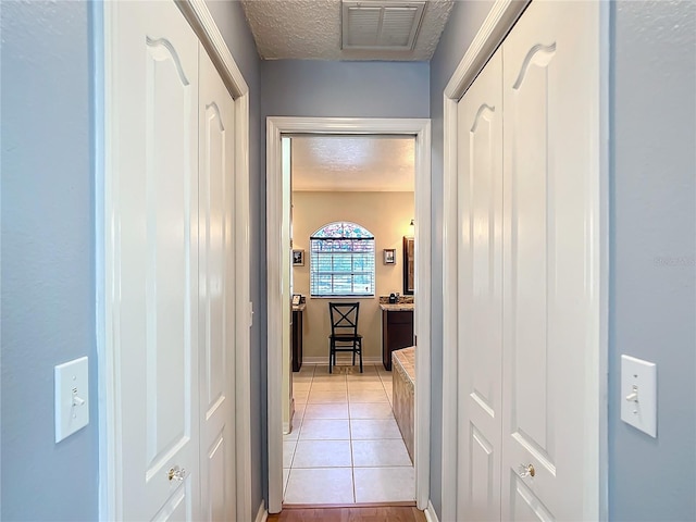 hallway featuring light tile patterned floors, visible vents, and a textured ceiling