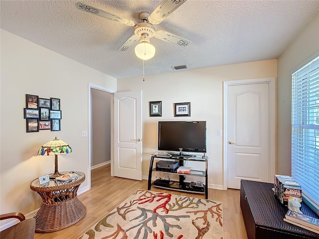 living room with a ceiling fan, baseboards, visible vents, and light wood finished floors