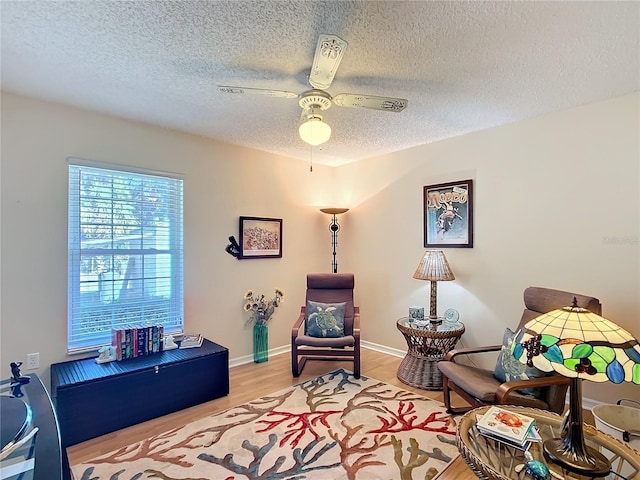 living area featuring light wood-style floors, a textured ceiling, baseboards, and a ceiling fan