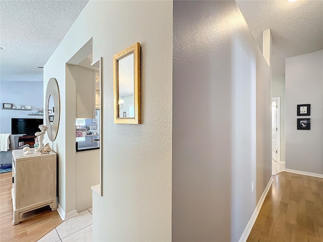 hall featuring a textured ceiling, light wood-style flooring, and baseboards