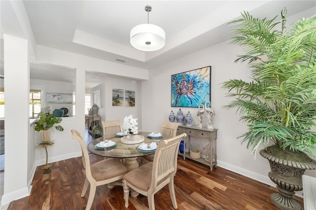 dining space featuring a tray ceiling, dark wood-style flooring, visible vents, and baseboards