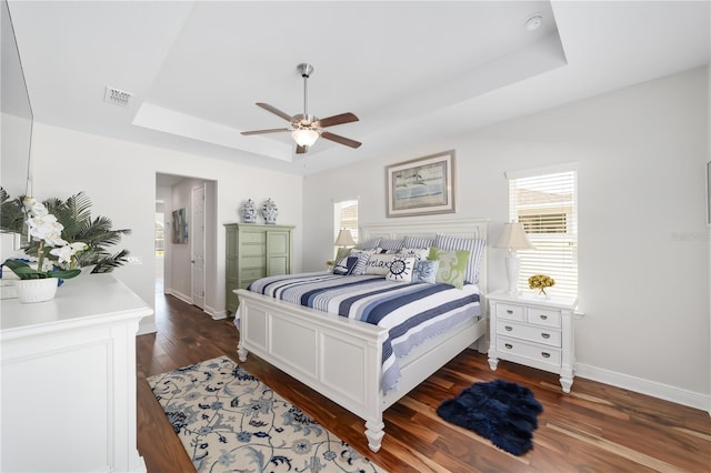 bedroom with visible vents, multiple windows, a tray ceiling, and dark wood-style flooring