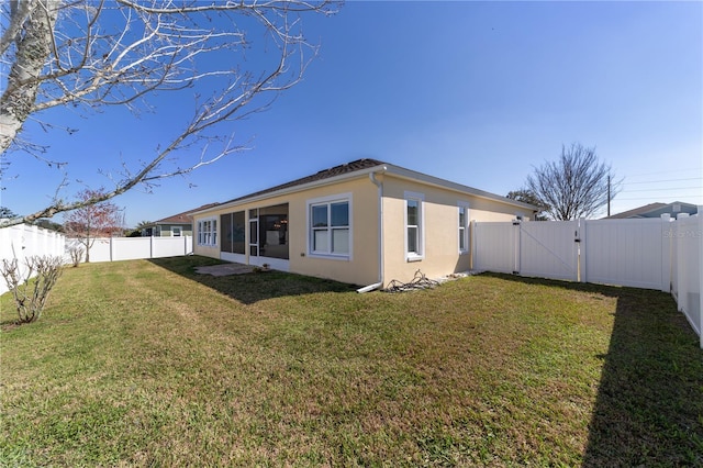 rear view of property featuring a yard, a fenced backyard, and a gate